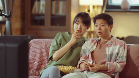 asian lesbian couple eating popcorn and watching tv at home