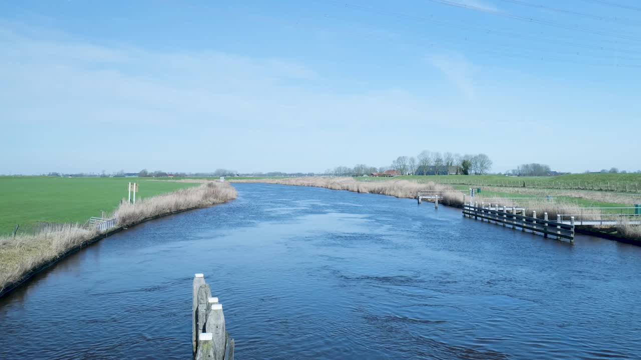 Breiter Fluss, der an einem sonnigen Tag durch grüne Felder strömt