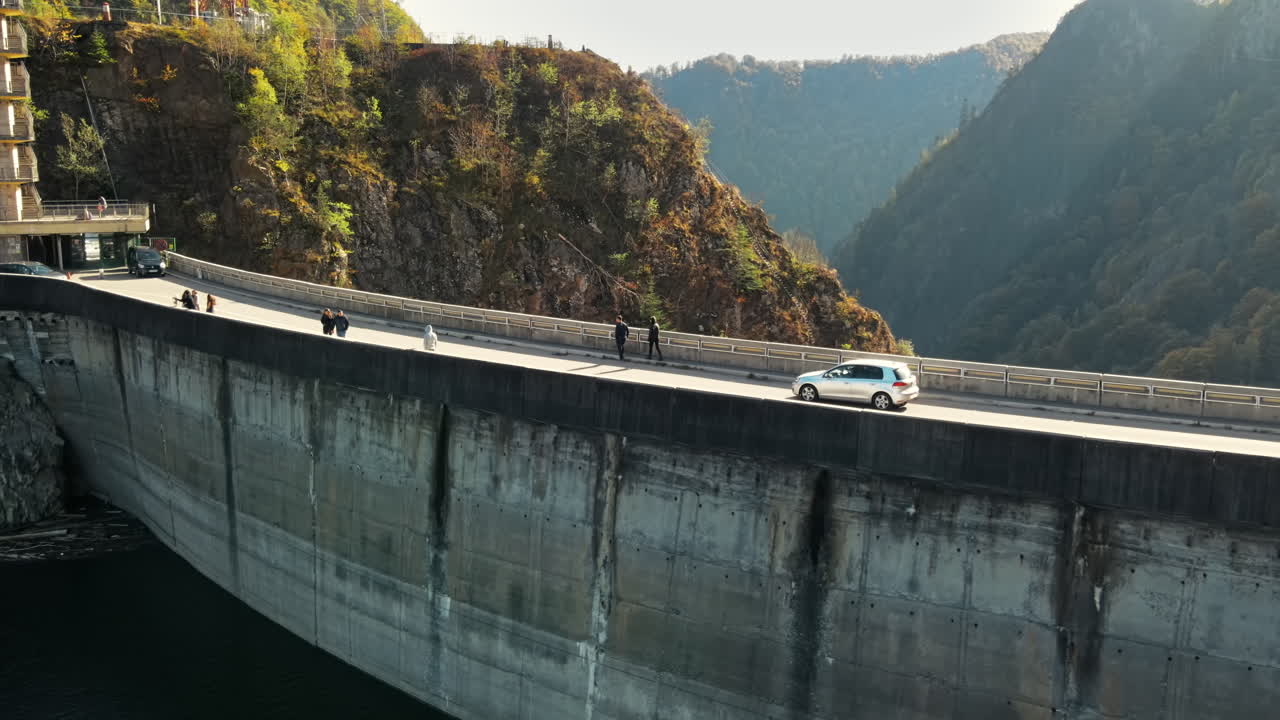 Aerial drone view of nature in Romania. Valley in Carpathian mountains with Vidraru dam, people and moving cars on it, slopes with lush forest