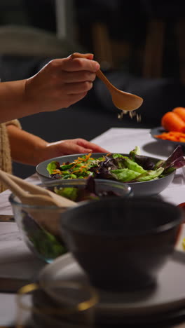 vertical video close up of woman at home in kitchen preparing healthy vegetarian or vegan meal mixing in seeds and dressing into bowl of salad leaves