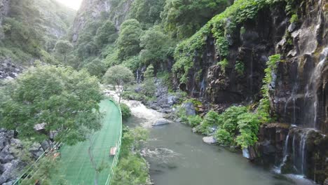 drone shot of a river flowing through a rocky gorge, surrounded by dense vegetation and steep cliffs, creating a dramatic and natural landscape