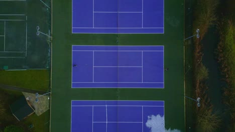 Toma-De-Drones-De-Arriba-Hacia-Abajo-De-Personas-Jugando-En-Una-Cancha-De-Tenis-Azul