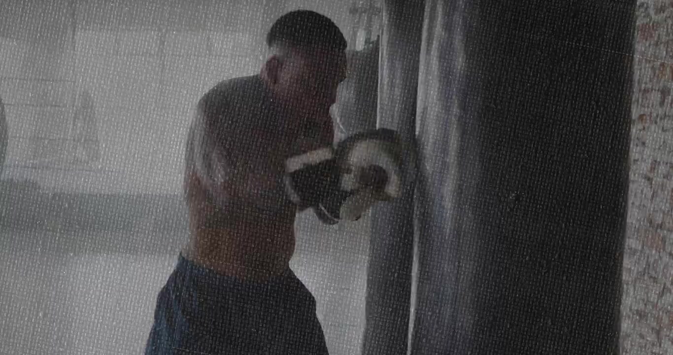 Pugile che preme il sacco pesante per stabilizzarlo, tirando indietro e sferrando jab, ruotando i fianchi per l'allenamento fitness
