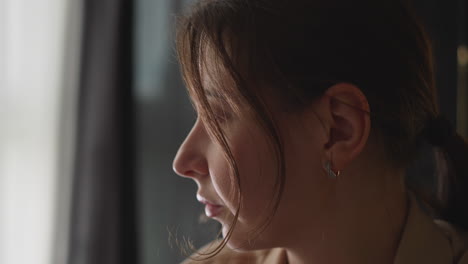 una joven triste hace un guiño mirando por la ventana desde la sala de estar