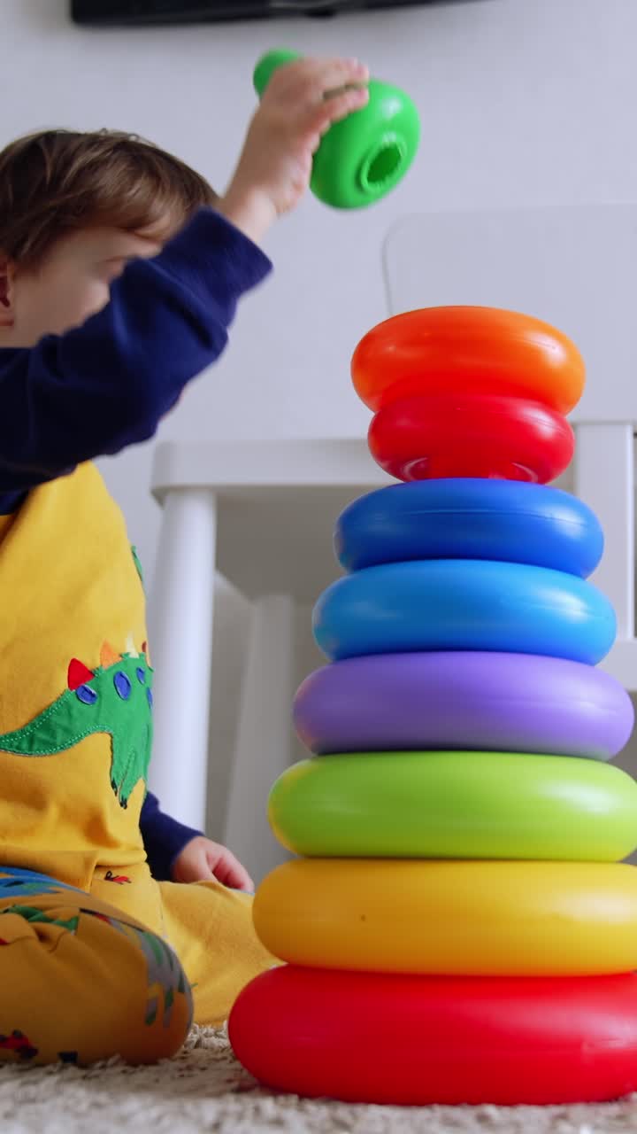 Niño pequeño adorable de dos años construyendo una pirámide en casa. El niño está sentado en el suelo, absorto en su juego. Vista de ángulo bajo.
