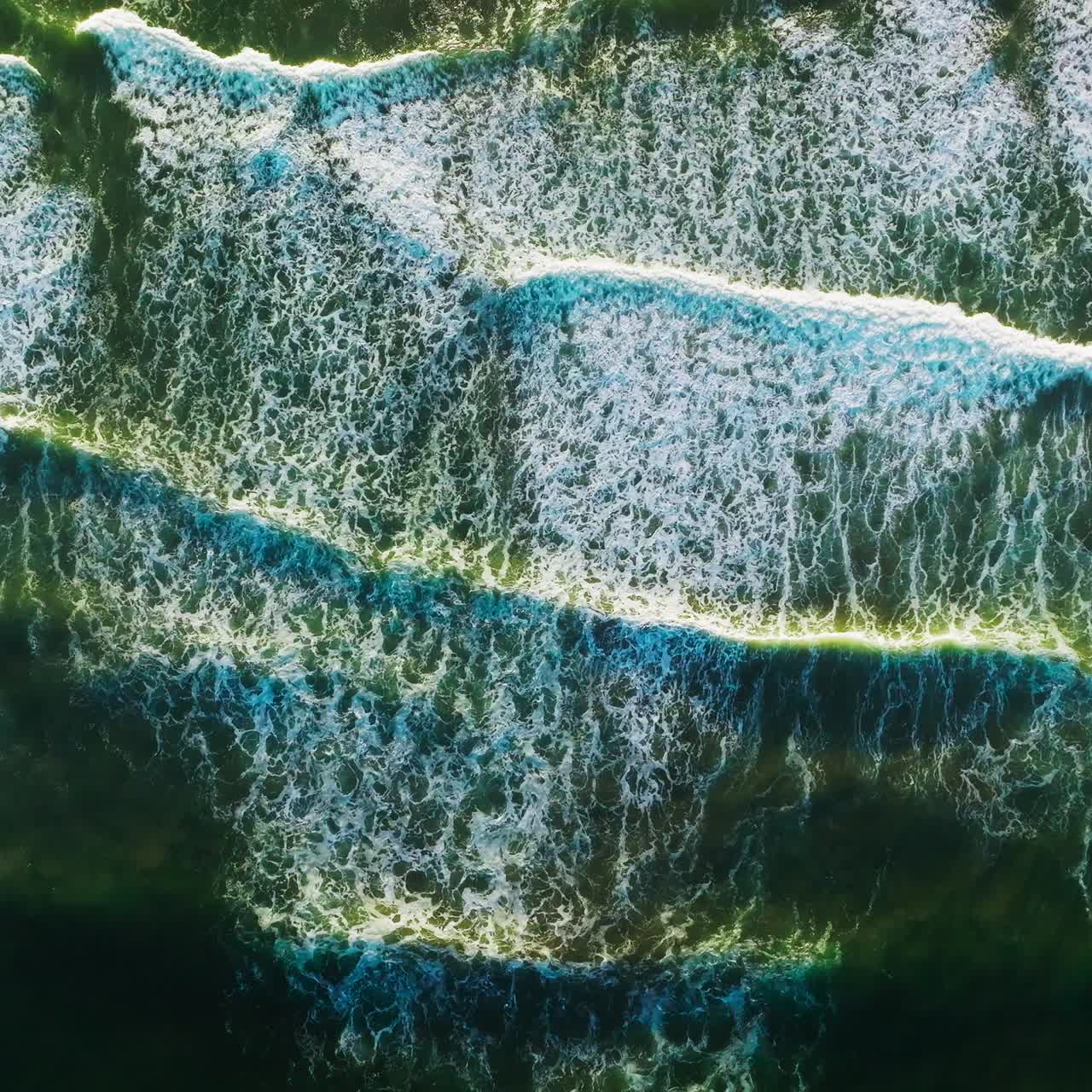 Beautiful relaxing movement of foamy waves on the surface of ocean. Descending drone footage over the deep green waters