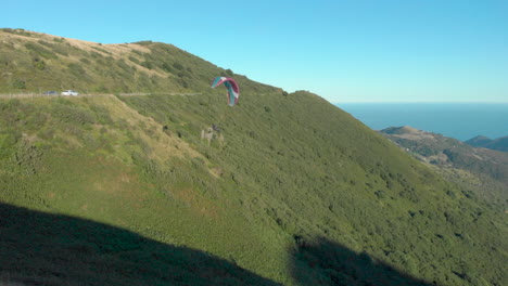 Aerial-paraglider-performs-stunts,-approaches-camera,-exits-left