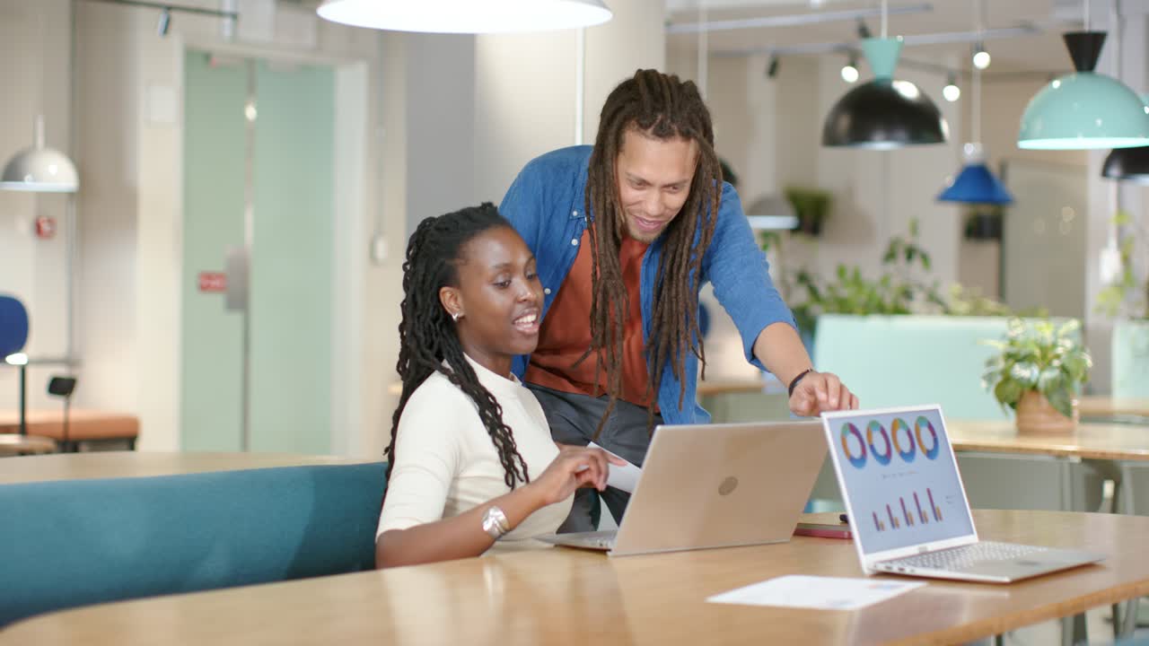 African American coworkers updating report at office, man approaching pointing, woman typing charts