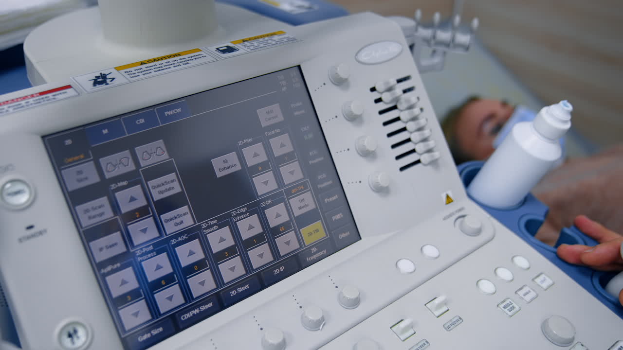 Touch screen and keyboard of ultrasound machine. Male medic applies ultrasonic device to a patient's belly. High angle view.
