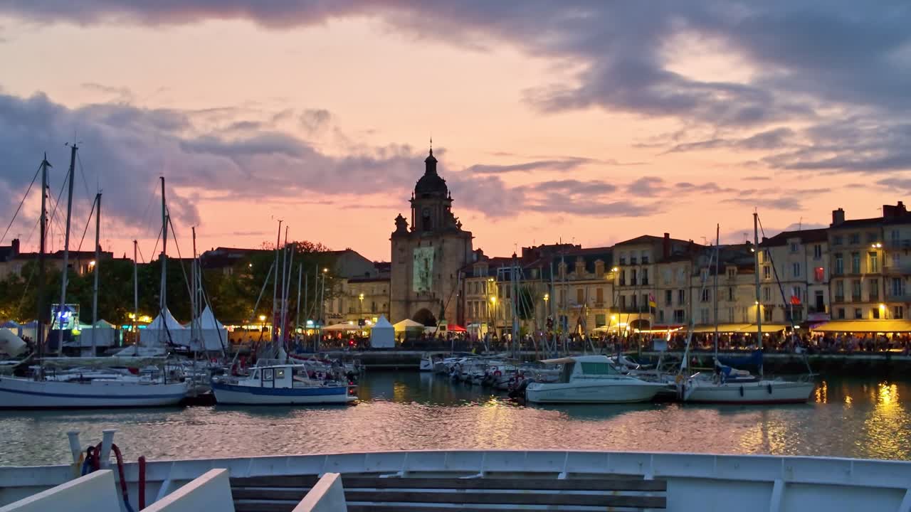 Old Port of La Rochelle at sunset, Grosse Horloge in background, sailboats moored in harbor under colorful sky, France
