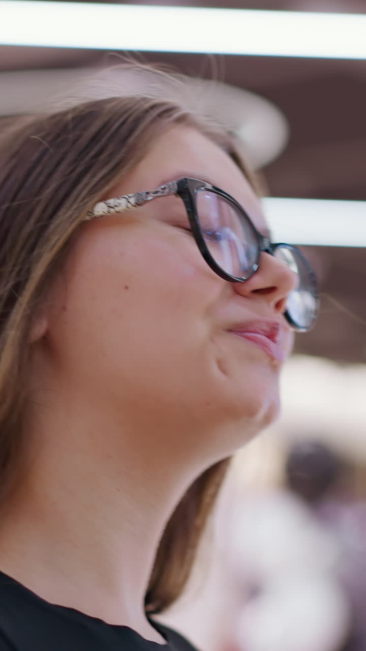 joven caminando con confianza por el centro comercial, usando gafas con fondo borroso de la tienda y figuras indistintas, mostrando un entorno de compras moderno y una experiencia de compras de moda