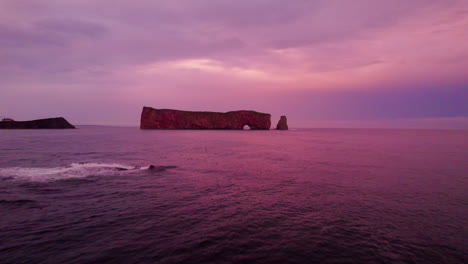 Vista-De-Drones-Alejándose-De-La-Roca-Percé-Durante-Una-Puesta-De-Sol-Nublada-Sobre-El-Río-San-Lorenzo