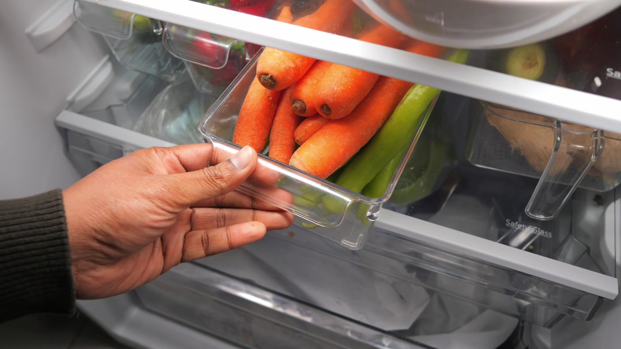 Hand Placing Fresh Carrots and Green Peppers into Refrigerator Drawer