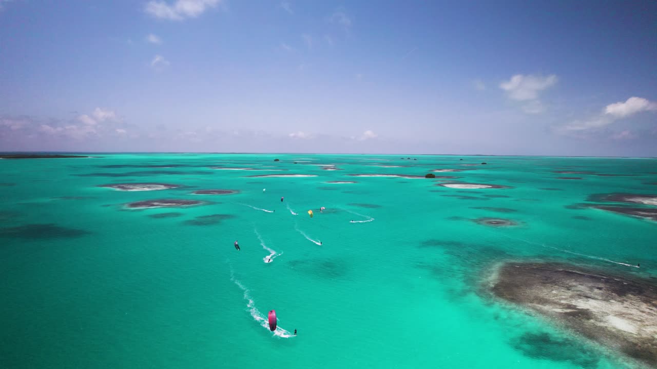Kite surfers glide over turquoise waters surrounded by small islands under a clear sky