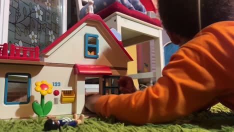 3-year-old black child playing with his toy house at home, lying on a green rug, wearing an orange long sleeve shirtj