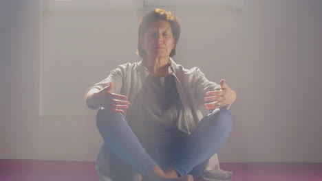 senior woman meditating in lotus position in gym