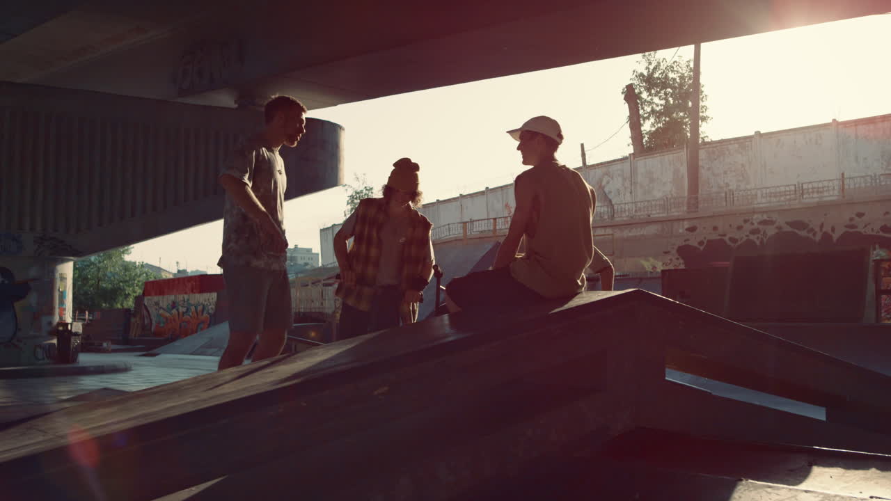 Stylish millennials relaxing skatepark. Hipsters talking together at sunset.