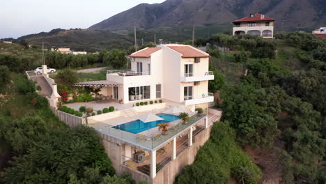 antena en sentido contrario a las agujas del reloj vuela alrededor de una lujosa villa griega con piscina con montañas en el fondo y follaje verde en primer plano - coche en marcha