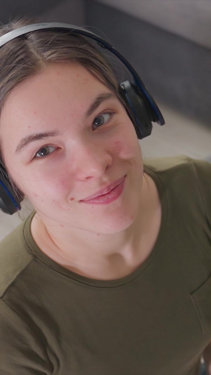 Il ritratto in primo piano mostra l'area dal viso alle spalle mentre qualcuno indossa cuffie over-ear. L'espressione del soggetto cambia sottilmente indicando il coinvolgimento con il contenuto audio. L'illuminazione soffusa crea