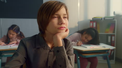 niño estudiando en el aula con sus compañeros de clase. estudiante masculino aburrido durante la lección