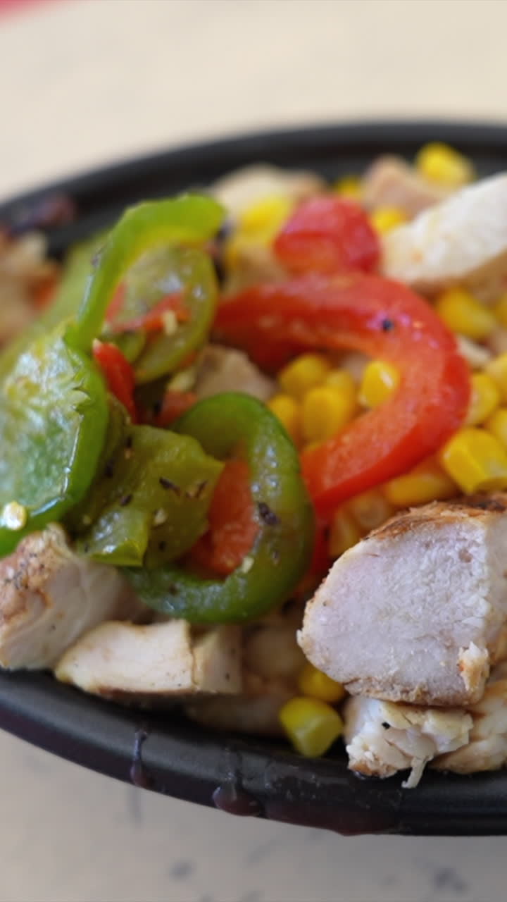 A vibrant close-up shot of a chicken and veggie bowl with colorful peppers, corn, and grilled chicken. Perfect for vertical video platforms, highlighting rich textures and appetizing colors