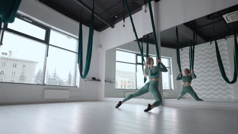 attractive fitness trainer doing antigravity aerial flying yoga exercises in green hammock. young flexible woman practice in aero stretching swing in fitness club. female fitness yoga routine concept