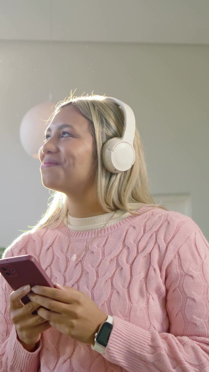 Video verticale: Toccando un telefono rosa, donna che si gira, ascoltando a casa in maglione, cuffie per la musica