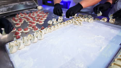 cooks in black gloves put ready-made ravioli on the tray. close up. dough circles with meat stuffing are laid in the table.