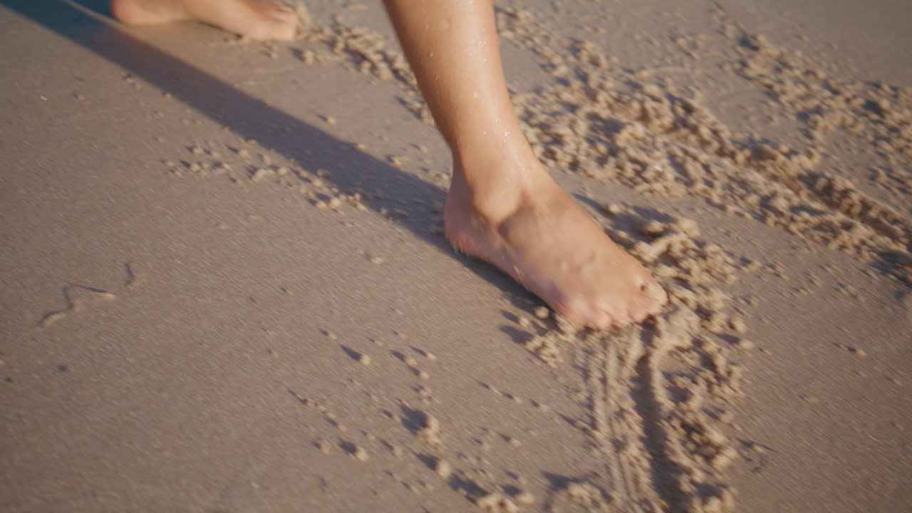Primo piano di gambe di donna che disegnano sulla spiaggia di sabbia. Piedi femminili abbronzati che creano impronte