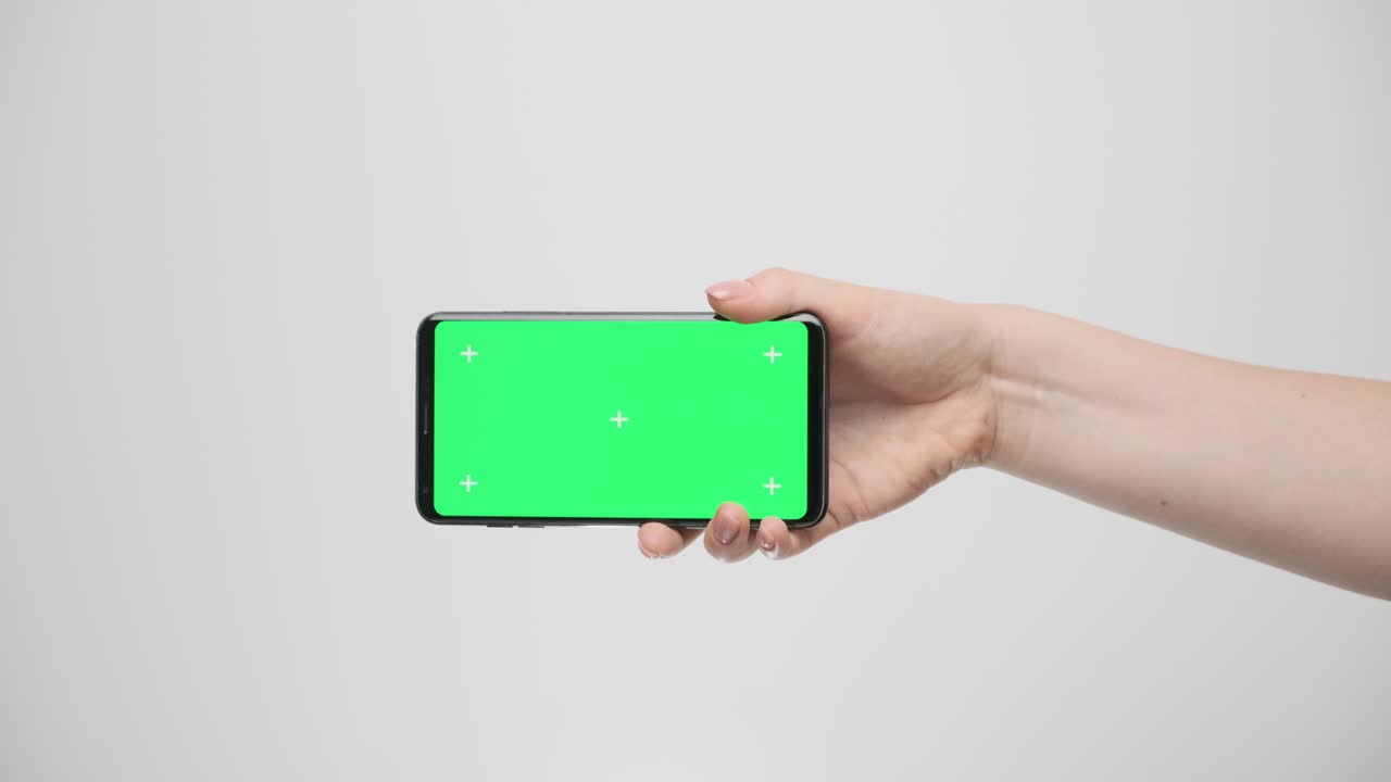 회색 배경에 있는 여성의 손에 녹색 화면이 있는 전화기입니다.