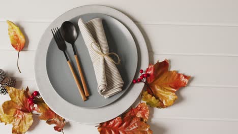 video of plate with cutlery and autumn decoration with leaves on white surface