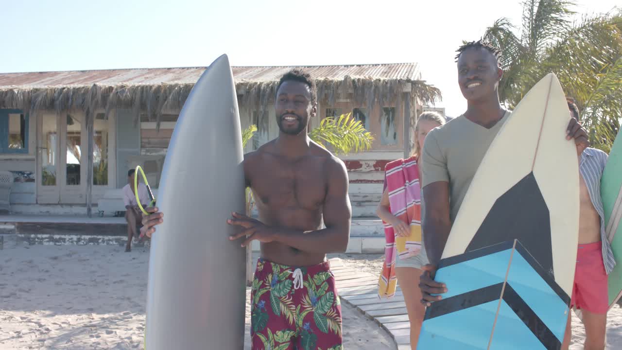 Felici amici eterogenei con tavole da surf che parlano con una casa al mare.