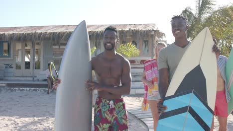 felices amigos diversos con tablas de surf hablando sobre la casa de la playa