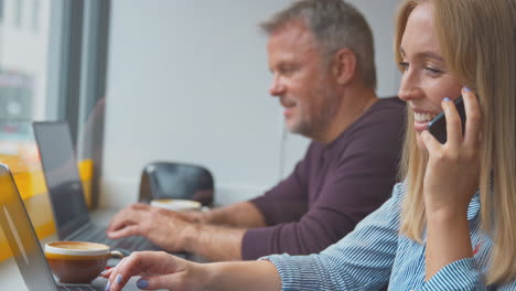 Clientes-En-La-Ventana-De-Una-Cafetería-Trabajando-En-Computadoras-Portátiles-Y-Haciendo-Llamadas-Por-Teléfono-Móvil