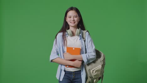 estudiante adolescente asiática con una mochila sosteniendo algunos libros y sonriendo mientras camina en el estudio de fondo de la pantalla verde