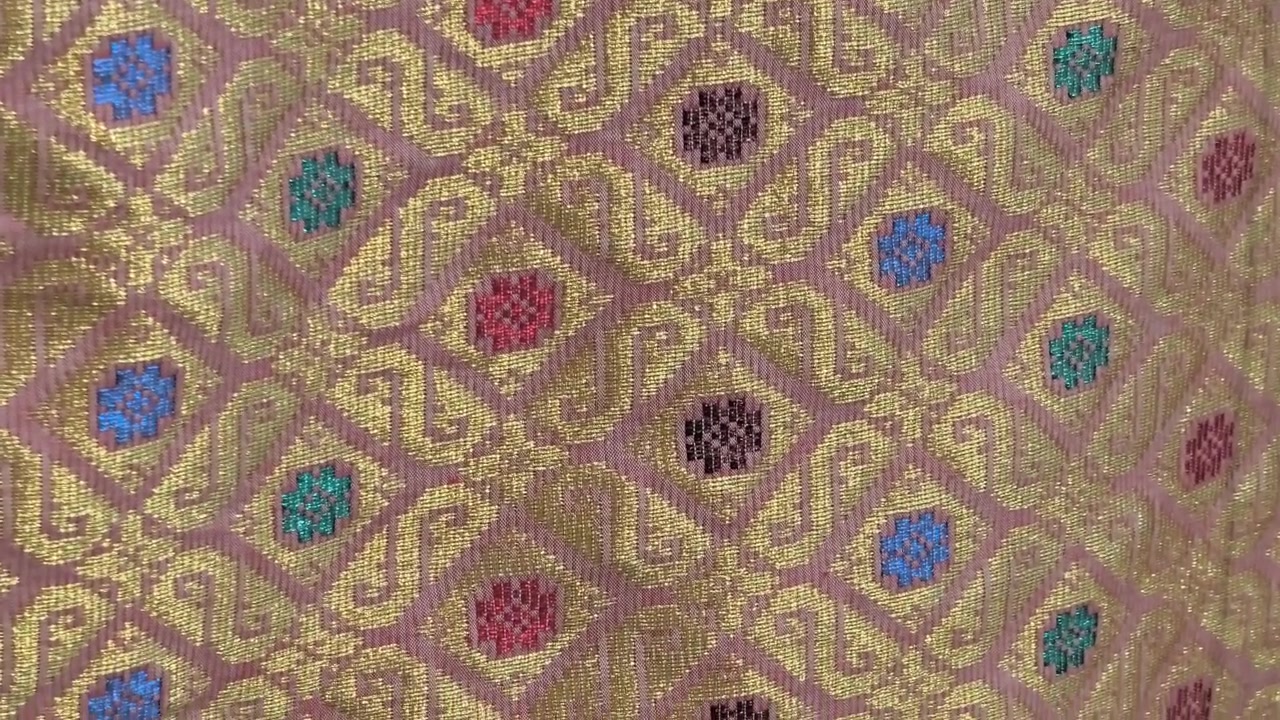 Primo piano dettagliato di lussuoso tessuto Songket. L'intricato ricamo dorato brilla sulla superficie tessuta a mano. Questo prestigioso tessuto malese è riservato alle occasioni più speciali.