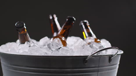 close up de una persona que toma una botella de vidrio refrigerada de cerveza fría o refrescos de un cubo lleno de hielo contra un fondo negro