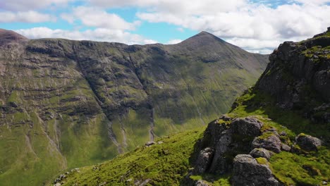 Aerial-Shot-around-Scottish-Mountains-Revealing-Herd-of-Deer-Walking-Along-Cliffside-of-Valley-in-the-Scottish-Highlands,-Scotland,-United-Kingdom