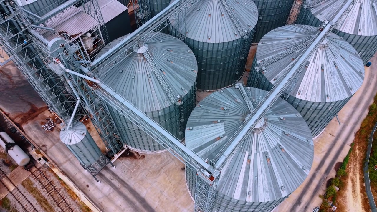 Large storage silos at a grain facility on a sunny day. These silos are used for grain storage in a large facility near train tracks.