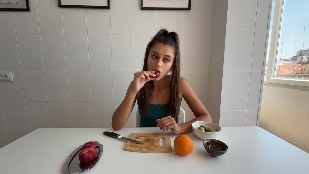 Young Woman Peeling and Eating Fresh Fruit in Kitchen
