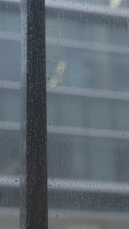 Real-rain-drops-sliding-on-window-glass,-vertical-view,-4K