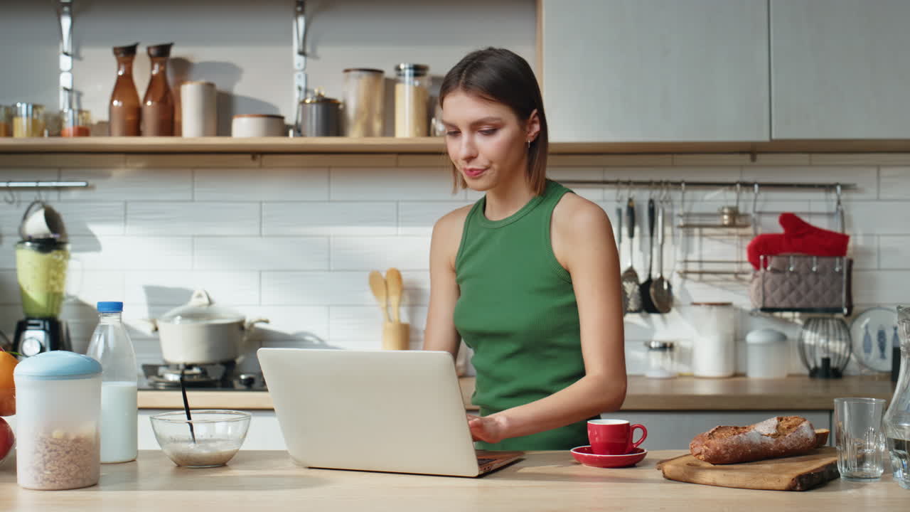 Woman using laptop in kitchen while having breakfast