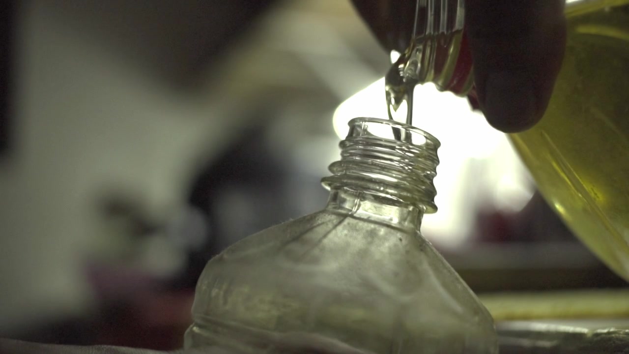 Close up of cooking oil being poured into a plastic bottle, highlighting ingredient transfer, food preparation and handling in an indoor kitchen environment
