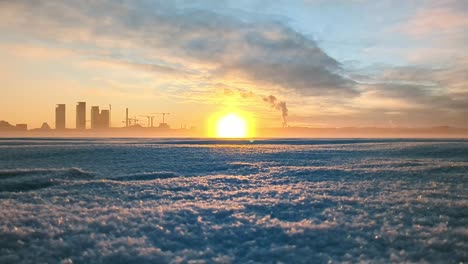 Gefrorenes-Meer-Bei-Sonnenuntergang-Mit-Skyline-Der-Stadt-Im-Hintergrund,-Atemberaubende-Winterlandschaft