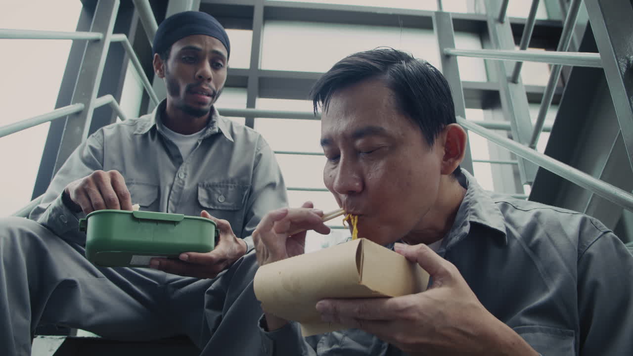 Two Construction Workers Having Lunch Sitting on Stairs