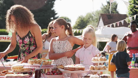 children serving on cake stall at busy summer garden fete