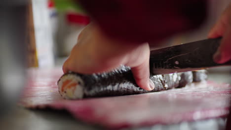 hands preparing sushi at home, slicing seaweed rice roll on red cutting board