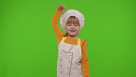 child girl kid dressed in apron and hat like chef cook baker raising hands, showing tasty gesture