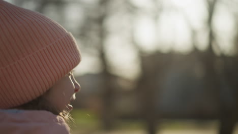 back view of a little girl wearing a pink cap and jacket, walking outdoors on a sunny day. the soft, warm light creates a peaceful and carefree atmosphere as she explores the surroundings