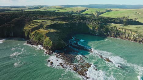 Aerial-view-of-wild-and-rugged-steep-cliff-coastline-with-rough-sea-and-crashing-waves-in-New-Zealand-Aotearoa